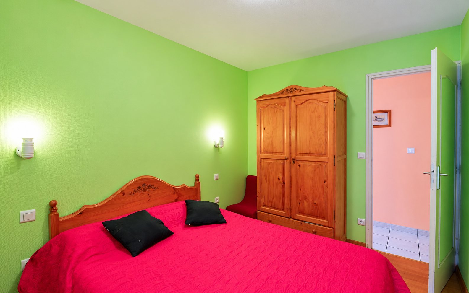 Chambre aux murs verts avec lit double rouge et armoire en pin