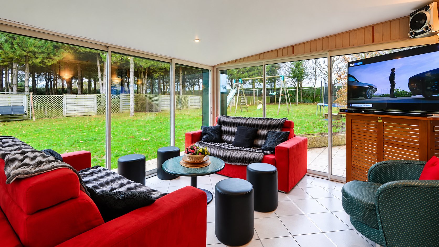 Salon vitré avec canapés rouges et vue sur le jardin